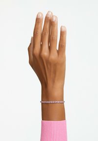 Rosa stensarmband på en brun hand, med runda stenar infattade i ett band i silverfärg. Handen är något lyft med utsträckta fingrar.