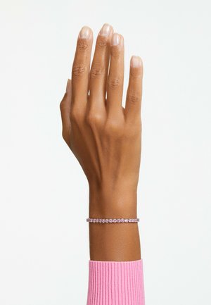 Bracelet en pierre précieuse rose sur une main brune, ornée de pierres rondes montées sur un bracelet en finition argentée. La main est légèrement levée avec les doigts étendus.