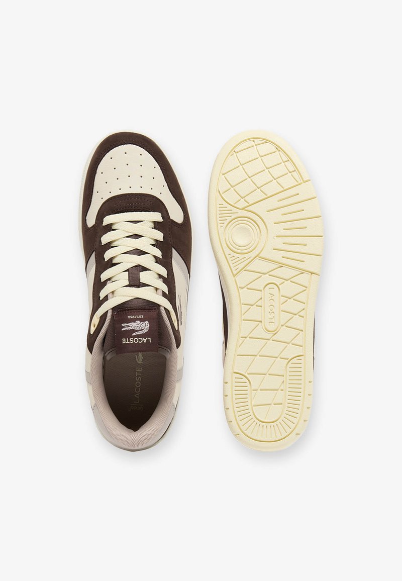 Brauner und cremefarbener Lacoste-Sneaker von oben mit gebundenen Schnürsenkeln, daneben passende cremefarbene, strukturierte Sohle, die nach oben zeigt.