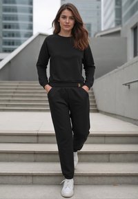 Svart sweatshirt och matchande sweatpants i ett mjukt material. Inkluderar sidfickor, elastiska muddar och vita sneakers.