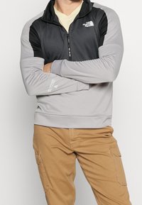 Pullover grigio e nero con zip, caratterizzato da un motivo testurizzato e maniche lunghe. Presenta il logo di The North Face sul petto e sulla manica.