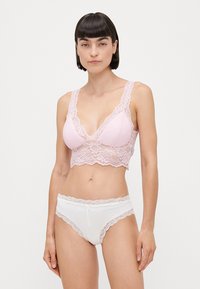 Lys rosa blonde bralette med v-hals og bølgede kanter, sammen med hvite truser med blondekant og frontknyting.