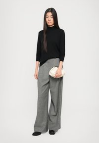 Schwarzes Langarmoberteil, graue weit geschnittene Hose und eine hellfarbene Clutch-Tasche. Glattes Material, lockerer Schnitt und minimalistisches Design ohne Muster.