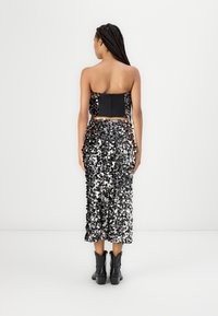 Top negro sin tirantes con un diseño ajustado, combinado con una falda midi de lentejuelas en negro y plata. Cuenta con un cierre de cremallera y un tejido texturizado.