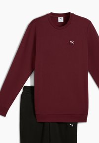 Weinrot Hoodie mit langen Ärmeln und Rundhalsausschnitt; mit einem kleinen weißen Puma-Logo-Patch. Kombiniert mit schwarzen Hosen, die über einen elastischen Bund verfügen.