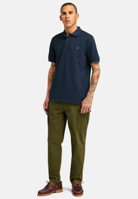 Polo navy de algodón, con cuello corto y logo bordado; combinado con pantalones cargo verde olivo y zapatos marrones.