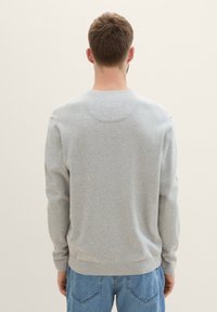 Sweatshirt gris à col rond, avec des poignets et un ourlet côtelés, texture douce et coupe décontractée, vu de derrière.
