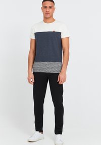 Marineblå og cremefarvet farveblokeret t-shirt med en tekstureret grå kant, parret med sorte bukser og hvide sneakers. Enkel, afslappet design.