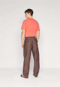 Camiseta de algodón roja de manga corta combinada con pantalones cargo marrones con bolsillos laterales y un ajuste relajado. Los zapatos son oscuros con rayas blancas.
