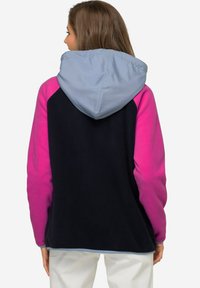 Giacca in pile con corpo blu navy, maniche rosa e cappuccio azzurro chiaro. Presenta una texture morbida e un'orlo elastico per una vestibilità aderente.