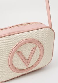 Μπεζ υφασμάτινη τσάντα με ροζ δερμάτινη επένδυση και ανάγλυφο κυκλικό λογότυπο. Διαθέτει κλείσιμο με φερμουάρ και ρυθμιζόμενο ροζ λουρί.