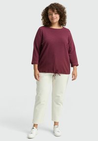 Haut à manches longues rayé bordeaux et maroon avec un col rond et un lien ajustable à la taille, associé à un pantalon cropped blanc et des baskets.