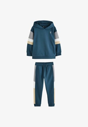 Børnesæt med mørk blågrøn hættetrøje og joggingbukser med grå, hvide og beige farveblokstriber på ærmerne og buksebenene.
