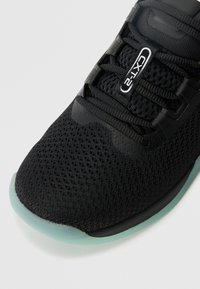 Czarne siateczkowe buty sportowe z czarnymi sznurówkami, etykieta "CXT-2" na języku oraz jasnoniebieski brzeg podeszwy na białym tle.