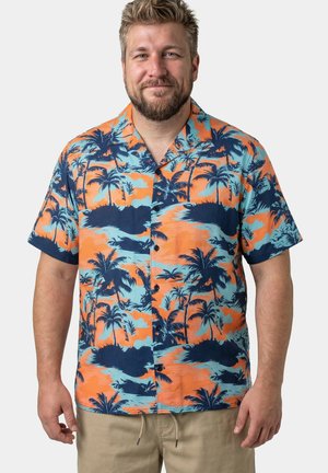 Mann trägt ein kurzärmliges orange-blaues tropisches Hemd mit Knöpfen und beige Hose, steht vor einem schlichten Hintergrund.