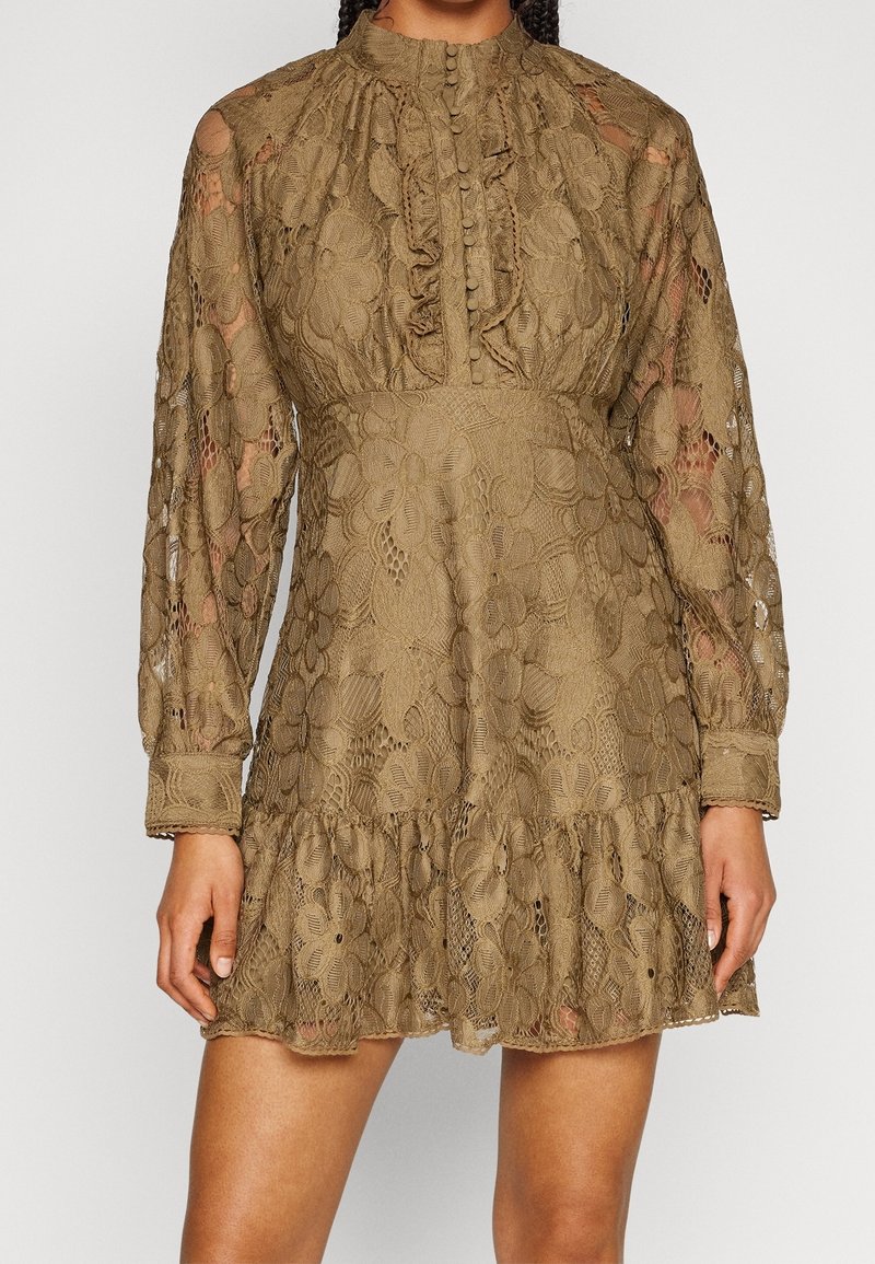 Robe courte en dentelle vert olive avec manches longues transparentes, col montant, devant à volants boutonné, taille cintrée et ourlet à volants.