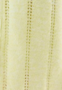 Miękka żółta dzianina z pionowymi wzorami ażurowych oczek rozmieszczonymi równomiernie na całej powierzchni materiału.