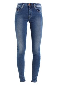 Smala jeans i blå denim, med medelhög midja, fem fickor och subtila blekningar längs benen. Kopparfärgad knappdetalj framtill.