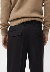 Pantalones negros con una textura suave, que cuentan con dos bolsillos traseros planos y un cinturón negro. Combinados con un suéter de punto acanalado en color beige.