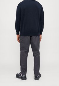 Pull marin avec un col rond et des manches longues, associé à un pantalon cargo gris avec poches latérales et des chaussures de sport noires.