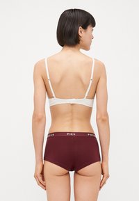 Vékony fehér pántos melltartó hátsó kapoccsal, amely bordó nadrággal párosul, fehér "PIECES" derékkal. Sima anyagú kivitel.