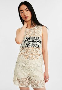 Blonde top med fine blomster mønstre, cremefarvet, uden ærmer, lagdelt tekstur, sammensat med matchende blonde shorts.