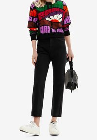 Farverig mønstret sweatshirt med primært grønne, lilla og røde farver, kombineret med sorte jeans med lige ben og hvide sneakers.