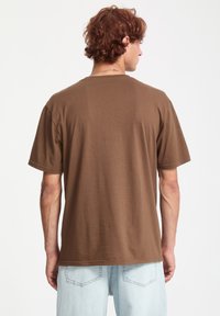 Brun bomulds t-shirt med afslappet pasform, korte ærmer og lige kant. Båret med lyseblå denim jeans, der viser et simpelt design.