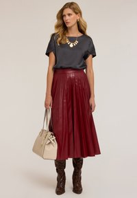 Blusa di raso grigio scuro, gonna in pelle rossa plissettata, borsa beige e stivali marroni con stampa serpente. Collana e orecchini in oro semplici.
