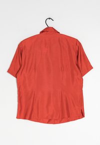 Red short-sleeved shirt with a collar, made of smooth fabric. Features a back slit and a hanging loop at the neck.