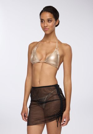 Top bikini triangolare metallico dorato con spalline a halter, abbinato a una gonna trasparente nera con glitter e lacci laterali regolabili.