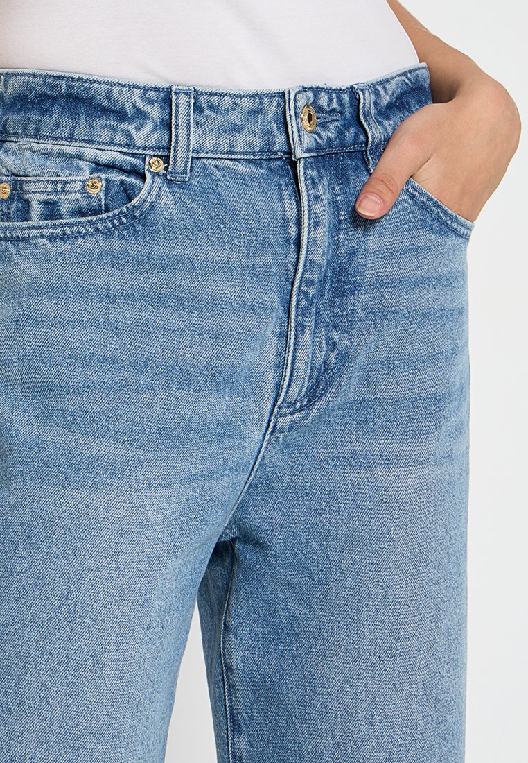 Jeans de mezclilla azul claro con una cintura alta, diseño clásico de cinco bolsillos, costuras visibles y una textura suave. Acentos de hardware en tono dorado.