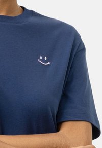 T-shirt à manches courtes bleu marine en tissu doux, avec un petit logo rose souriant sur la poitrine gauche.