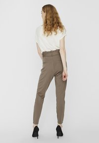 Beige housut, joissa on korkea vyötärö, kaksi takataskua ja kapeat lahkeet, yhdistettynä löysään valkoiseen paitaan ja mustiin korkokenkiin.