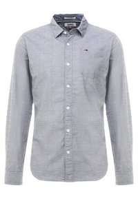 Šedá košile na zapínání s dlouhým rukávem, texturovaným materiálem, bílými knoflíky a náprsní kapsou. Na kapse je malé logo.