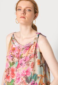 Blusa sem mangas floral com decote franzido, apresentando padrões vibrantes de rosa, laranja e verde em tecido leve e transparente. Alças ajustáveis nos ombros.