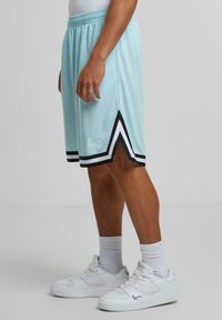Shorts de basket bleu clair avec des rayures d'accent noires et blanches, présentant une conception à ourlet fendu. Associés à des baskets blanches et des chaussettes montantes.