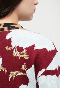 Suéter de malha com um padrão floral em bordô e azul claro, com um colarinho em estampa de leopardo. Textura macia com um design de gola redonda.