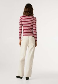 Langsleeve ribbel top met rood-witte horizontale strepen, gecombineerd met crèmekleurige wijde broek en zwarte hoge hakken.