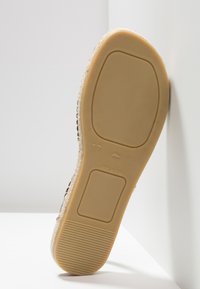 Semelle d'une espadrille femme taille 37 avec semelle extérieure en caoutchouc, talon texturé, et semelle intermédiaire en corde tissée, positionnée contre un mur blanc.