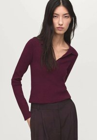Pull en tricot bordeaux avec col, coupe ajustée, manches longues et texture douce, associé à un pantalon sombre et ajusté.