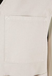 Gros plan d'une poche en tissu beige avec des coutures visibles sur un vêtement, montrant la texture et les bords cousus.