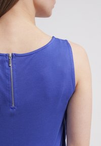 Hiatonen, violetti mekko, jossa on selkävetoketju ja sileä kangaspinta. Kaula-aukko on pyöreä, ja saumat ovat siististi viimeistellyt.