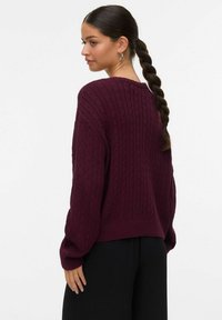 Maglione bordeaux lavorato a maglia con design a cavo testurizzato, vestibilità rilassata e polsini a costine. Caratterizzato da un collo a barca e maniche larghe.