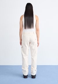 Beige cargobukser med striber lavet af bomuld, der har sideposer og en afslappet pasform, parret med en hvid tanktop og sorte sko.