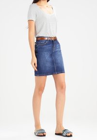 Jeansowa spódnica z rozcięciem z przodu, niebieska, zestawiona z pasiastą bluzką z krótkim rękawem i brązowym paskiem. Obuwie to wzorzyste klapki.