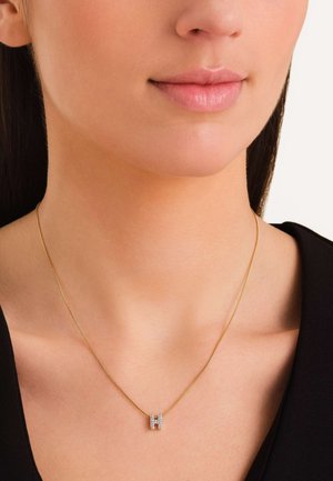 Collar de oro con un pequeño colgante en forma de letra 'H' adornado con diamantes, cadena delgada y un acabado suave y pulido. Se lleva cerca del cuello.