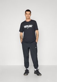 T-shirt nera Nike con testo bianco che recita "VINCERE INIZIA CON L'ALLENAMENTO," abbinata a pantaloni sportivi neri e scarpe da ginnastica nere.