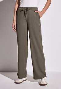 Lichte, getextureerde olijfgroene broek met een wijde pijp, een trekkoord in de taille en zijzakken, gedragen met crèmekleurige sneakers.