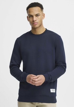 Marineblauwe sweatshirt van zacht materiaal met een geribbelde ronde hals en manchetten; heeft een label aan de onderzijde aan de linkerkant.
